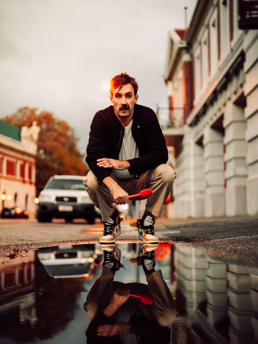 Sev crouched on a wet street, reflected in a puddle